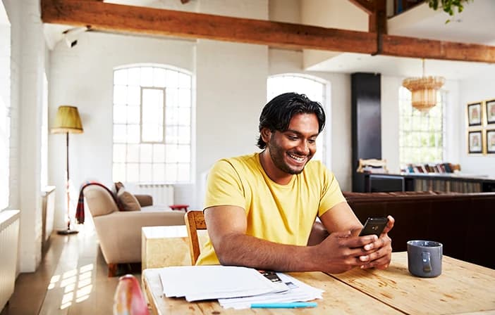 Man sitting at table in well-lit room, smiling and looking at his phone