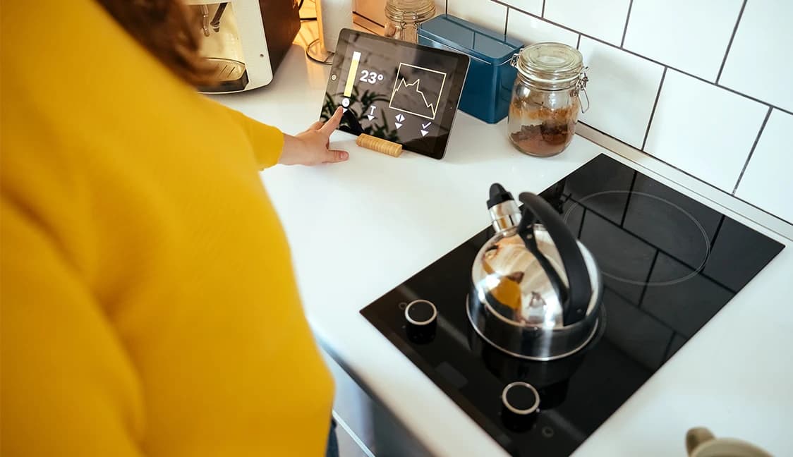 Kettle on electric stove top with person using table to monitor power usage.