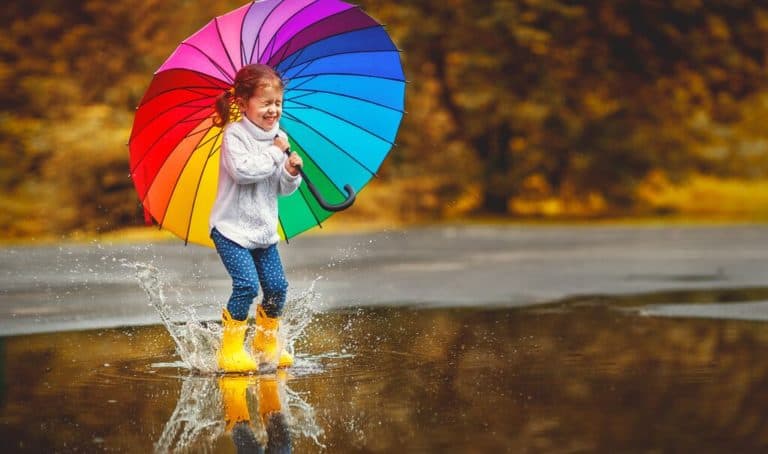 Girl with colourful umbrella jumping in puddle
